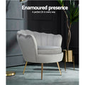 Light grey velvet scallop shell armchair with gold legs in dark moody room with plant in gold pot, Enamoured presence text