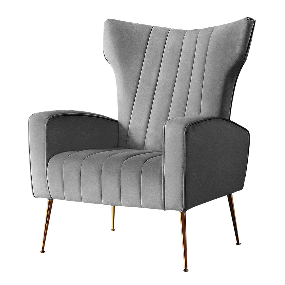 Grey velvet wingback armchair with tall winged back and vertical channel stitching angle view on white background