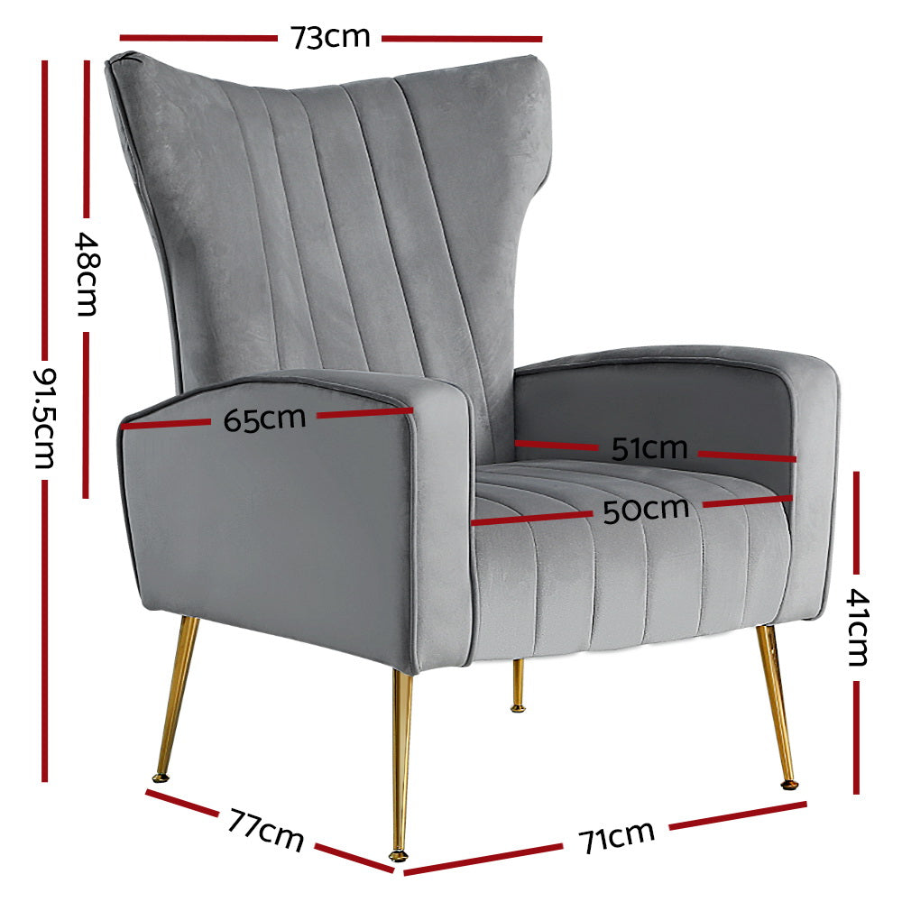 Grey velvet wingback armchair with vertical channel stitching and gold metal legs in living room lifestyle scene