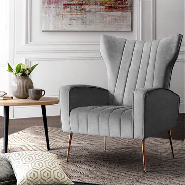 Grey velvet wingback armchair with vertical channel stitching and gold metal legs in living room lifestyle scene