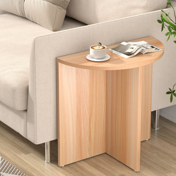 Half-moon side table in natural oak with cross-shaped base and metal feet, beside beige sofa, coffee cup and magazine on top
