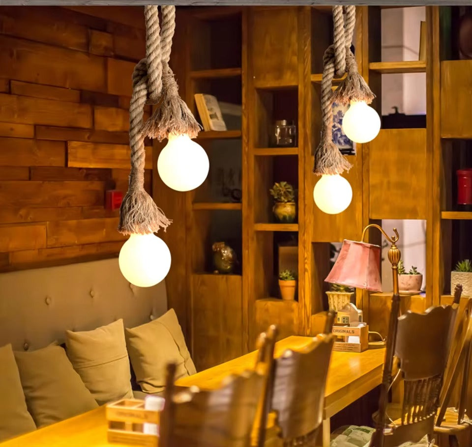 Two hemp rope pendant lamps with round globe bulbs in rustic cafe, wood panelled shelves and seating in background