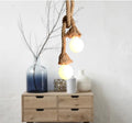 Hemp rope double pendant with two frosted globe bulbs glowing above wooden drawers, blue vase with branches and ceramic vases