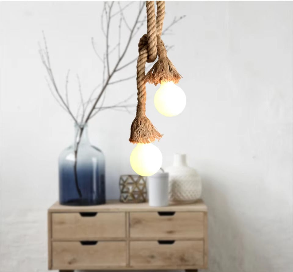 Hemp rope double pendant with two frosted globe bulbs glowing above wooden drawers, blue vase with branches and ceramic vases