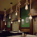 Hemp rope pendant lights with Edison bulbs hanging in rustic restaurant with green walls and dark wood tables