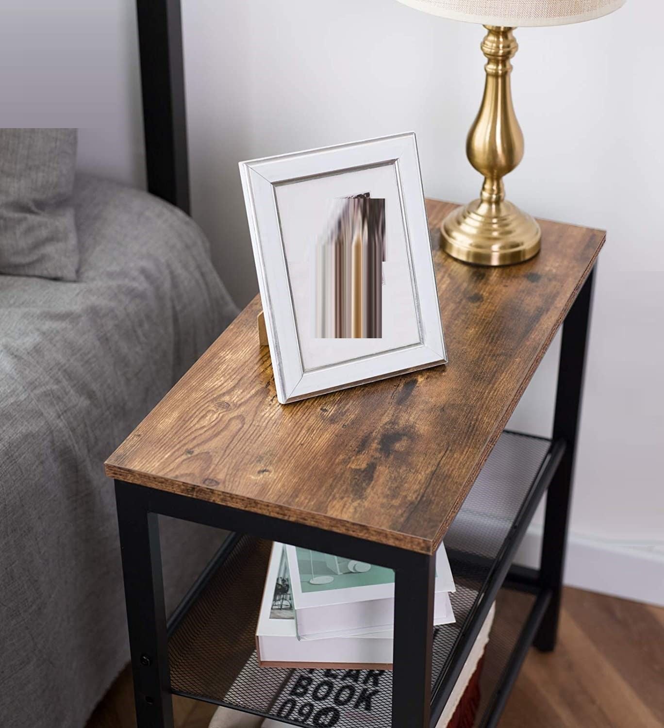 Industrial side table close-up in bedroom with photo frame and brass lamp on rustic wood top, books on shelf