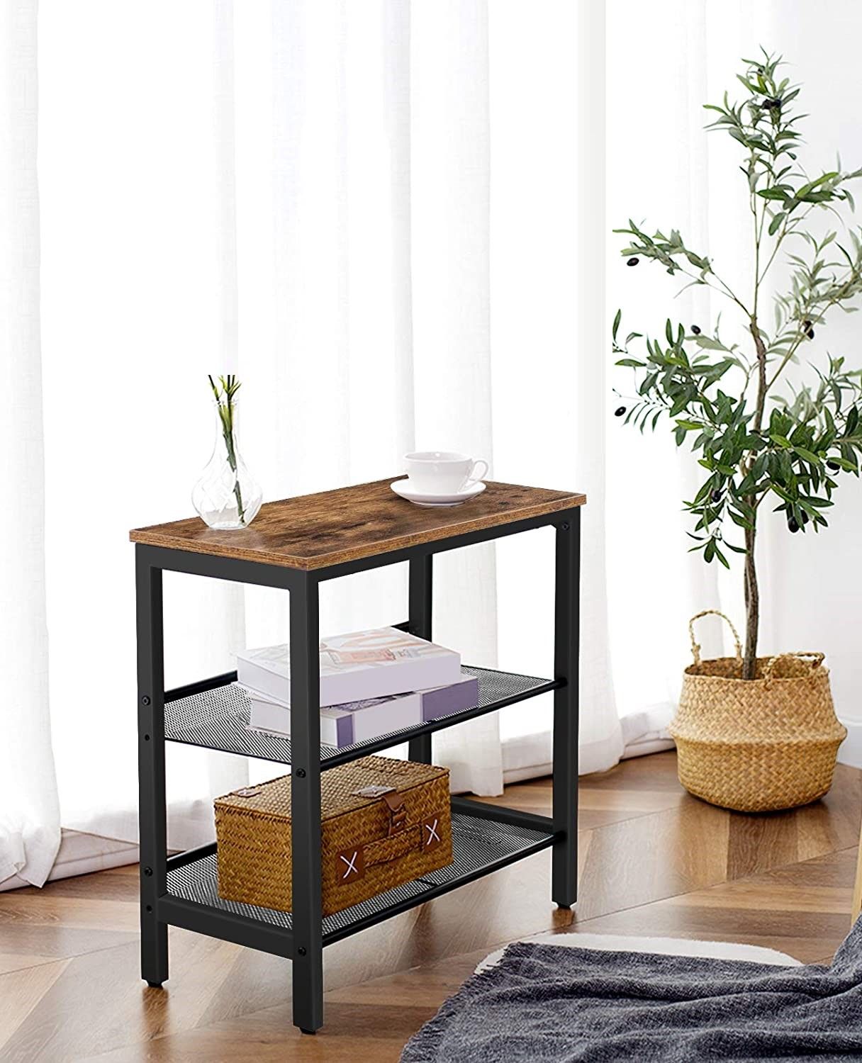 Industrial side table beside curtained window, glass vase on top, books and basket on shelves, plant nearby