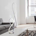 Chrome infinity LED floor lamp beside grey sofa, smaller table version on coffee table in foreground, window and chair behind