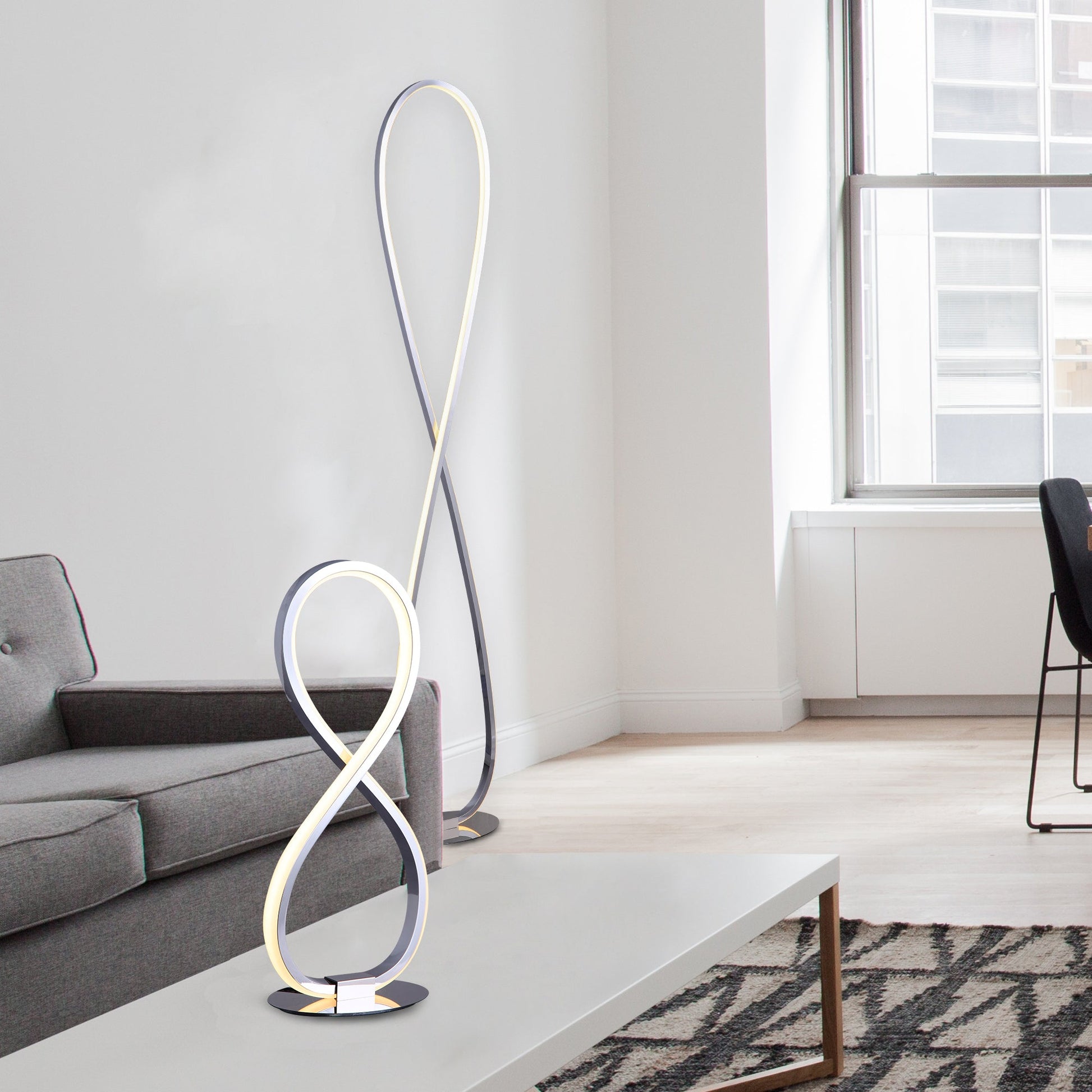Chrome infinity LED floor lamp beside grey sofa, smaller table version on coffee table in foreground, window and chair behind