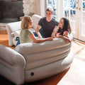 Three people sitting on beige inflatable corner sectional sofa in living room with brick fireplace
