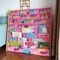 Pink fabric book display rack filled with children's books in room, front angle, decorative screen and sofa visible