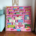 Pink fabric children's book display rack filled with picture books in room setting next to teal sofa and decorative screen