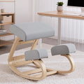 Grey fabric kneeling rocker chair on white shag rug next to standing desk and shelving unit, angle view
