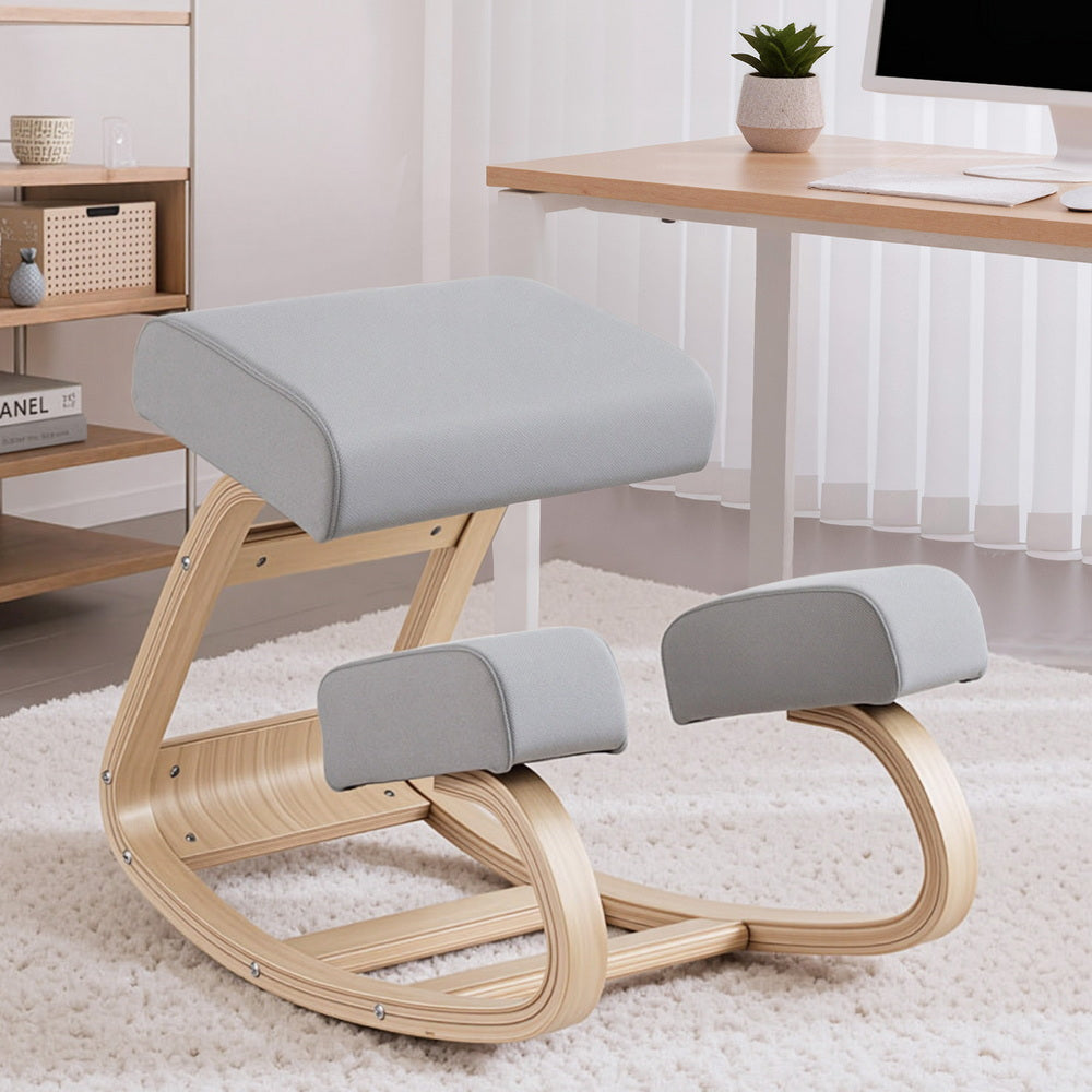 Grey fabric kneeling rocker chair on white shag rug next to standing desk and shelving unit, angle view