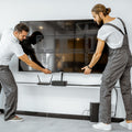 Two workers lifting large TV to wall bracket mount in white room one in overalls one in white t-shirt