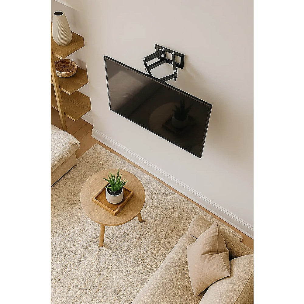 Small full-motion TV wall bracket lifestyle with TV tilted on cream wall oak bookshelf round coffee table and plant