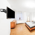 Large TV wall-mounted on full-motion bracket in white bedroom with pine dresser white curtains and wood-frame bed