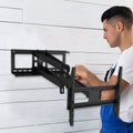 Man in blue overalls mounting large full-motion TV wall bracket onto white wooden plank wall