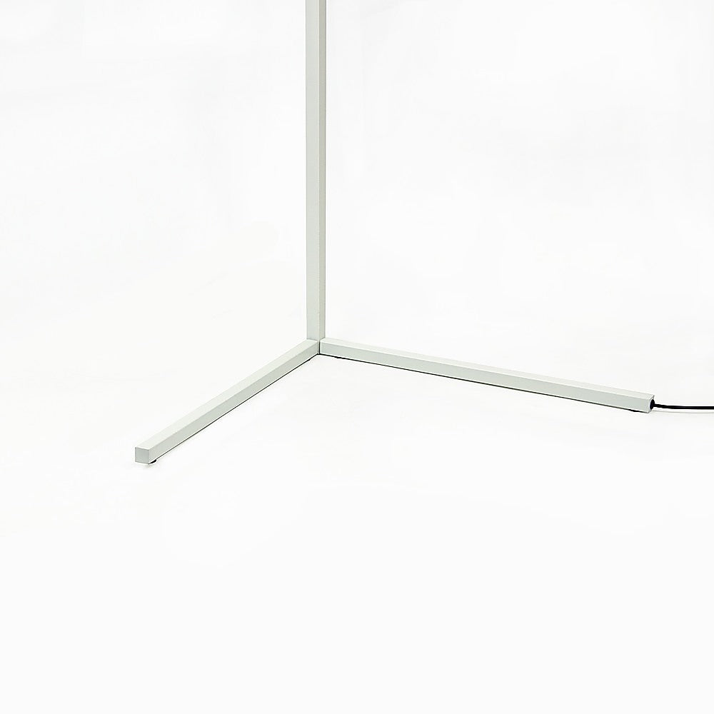 Close-up of white square-section tripod base of LED floor lamp with black power cord on white background