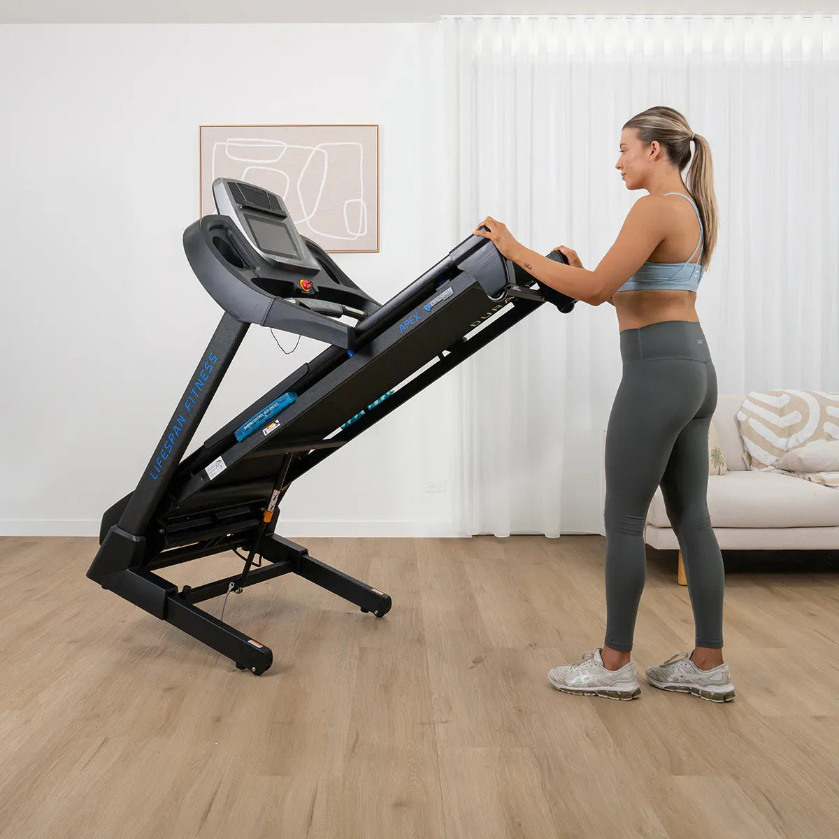 Woman using Lifespan Apex 2 at incline position with hands on handrails in home fitness setting