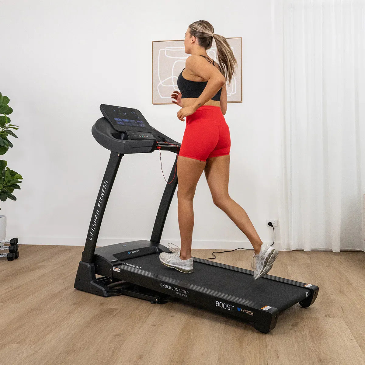 Woman running on Lifespan Boost 2 in home gym with wooden floor and plant