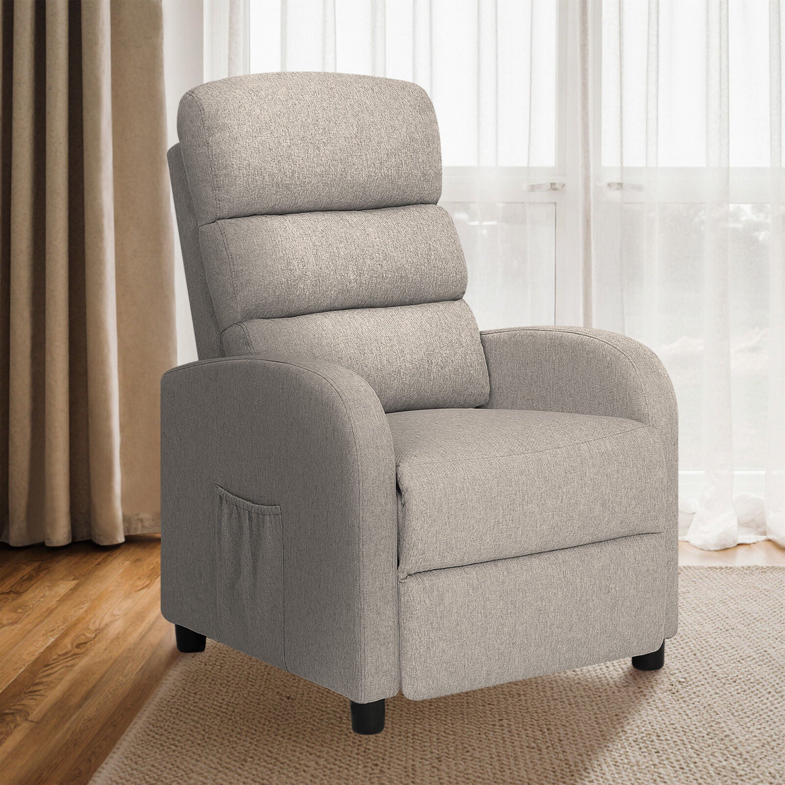 Light grey fabric recliner upright in living room with sheer curtains, wooden floor and rug, three-quarter angle