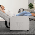 Woman reclining in light grey fabric chair with footrest extended, side pocket visible, living room background