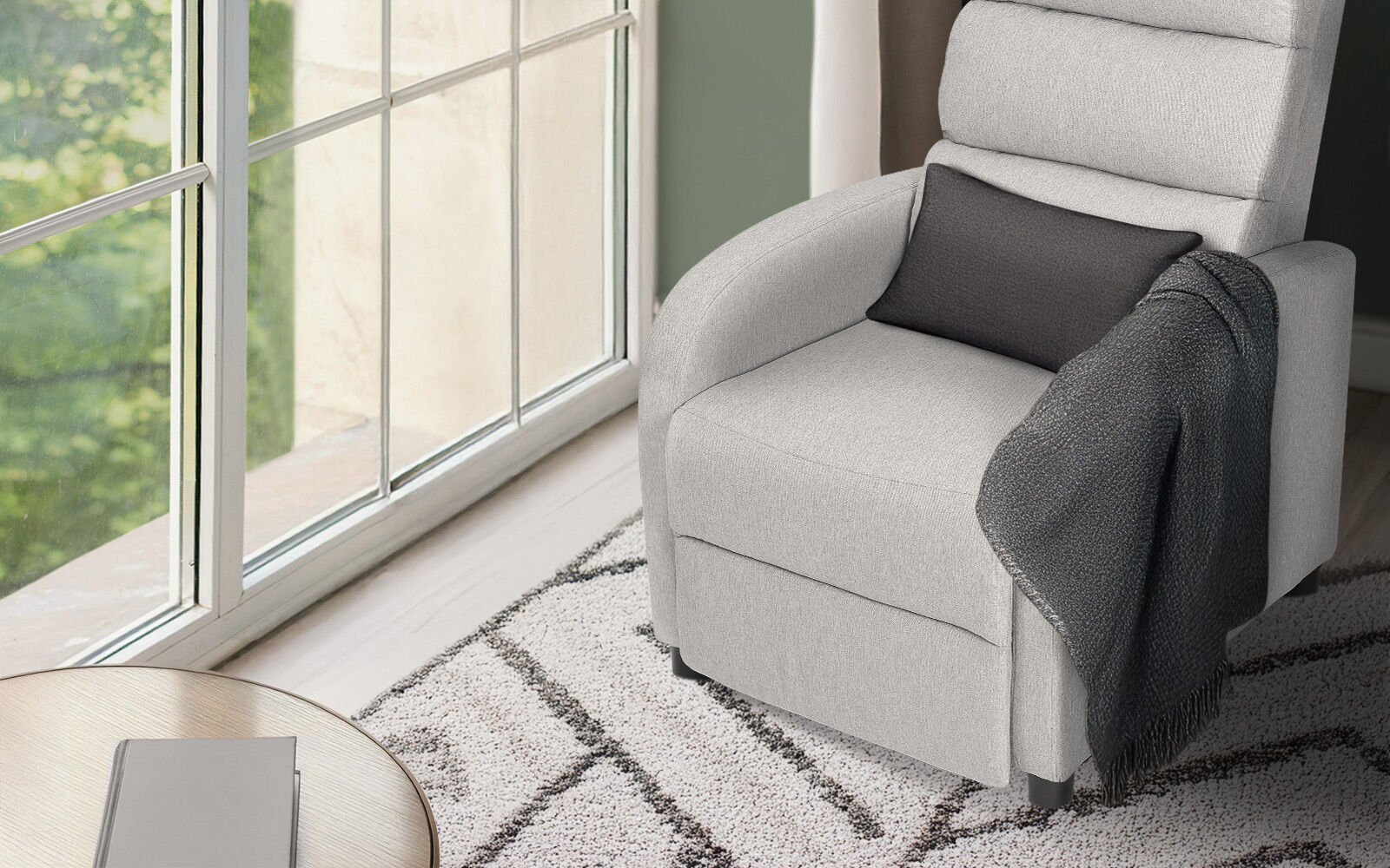 Light grey fabric recliner upright beside large window with dark grey cushion and throw, patterned rug, round coffee table