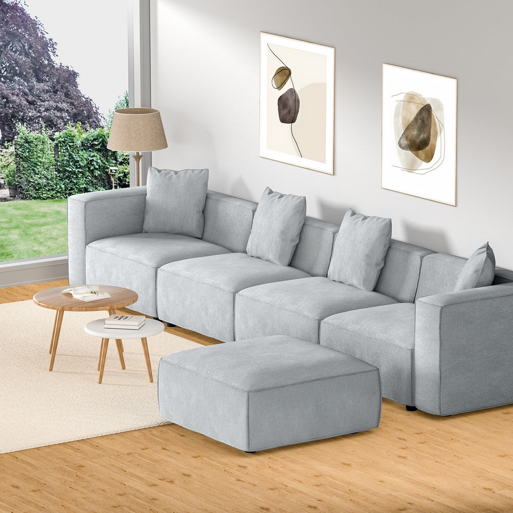 Light grey modular 4-seater sofa with ottoman in bright living room with garden window view