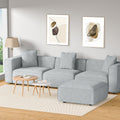 Light grey modular sofa with ottoman in Scandinavian-style room with wooden tables and abstract wall art