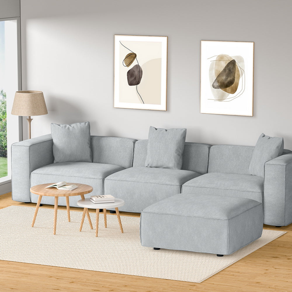 Light grey modular sofa with ottoman in Scandinavian-style room with wooden tables and abstract wall art