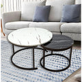 Two round nesting marble coffee tables with bronze ring bases styled in front of grey sofa with blue cushions on patterned rug