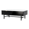Coffee table with white marble top, black ribbed drawer with gold handle and open shelf, black metal legs, white background