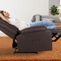 Woman fully reclined in dark brown PU leather recliner chair with footrest extended on orange rug in living room