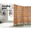 Natural 8-panel louvered wood room divider with shelves in lifestyle room with orchid plant framed art and light wood floor