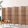 Natural 8-panel woven paper rope room divider in lifestyle room with rattan chair and tropical plant against white wall