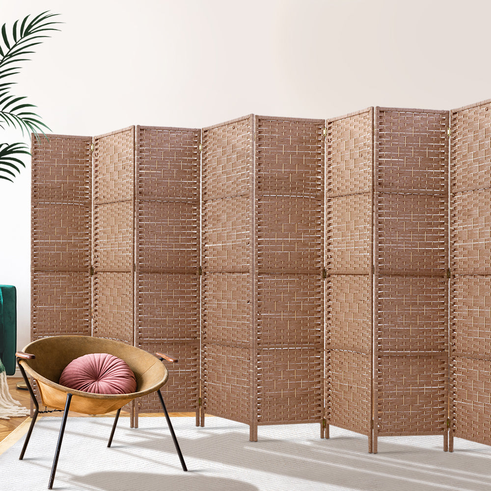 Natural 8-panel woven paper rope room divider in lifestyle room with rattan chair and tropical plant against white wall