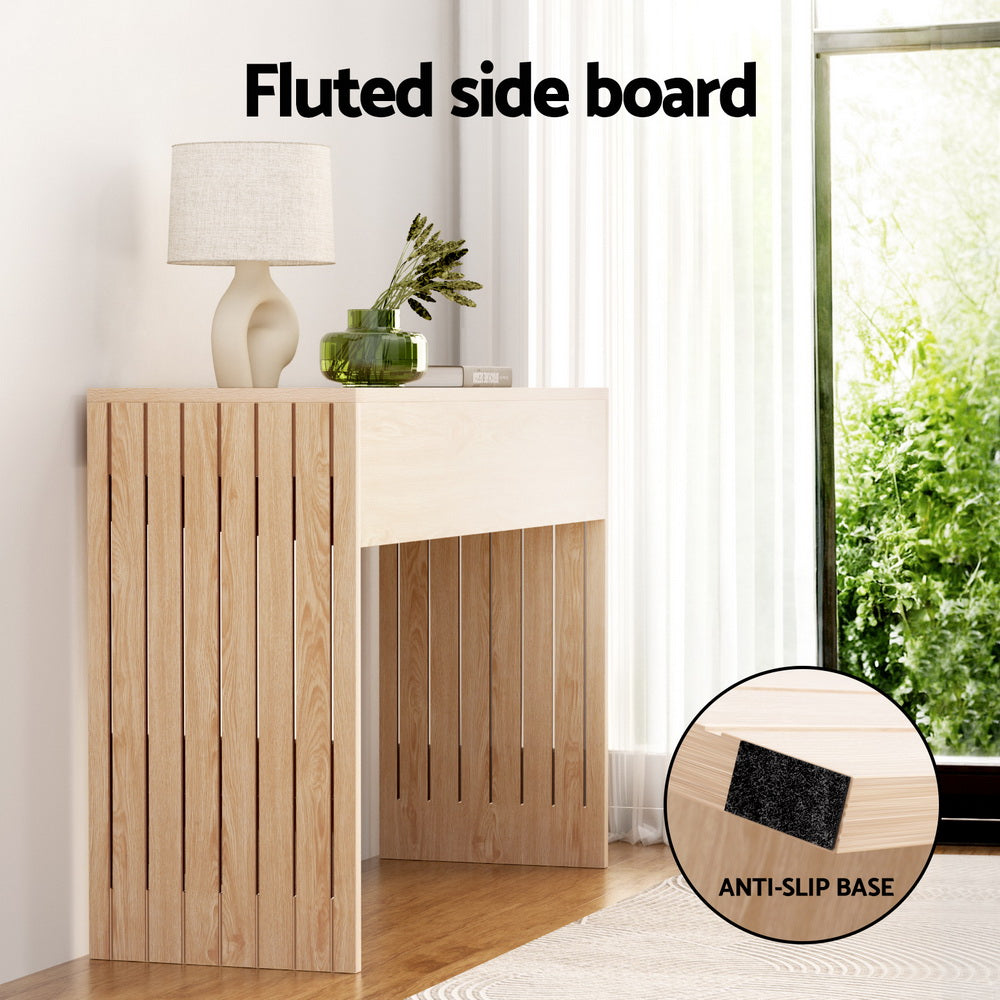 Natural oak console table with fluted side boards in windowed room, lamp and vase on top, close-up shows anti-slip base pad