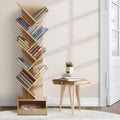 Natural wood tree bookshelf filled with books in neutral room with wooden side table, three-quarter angle view