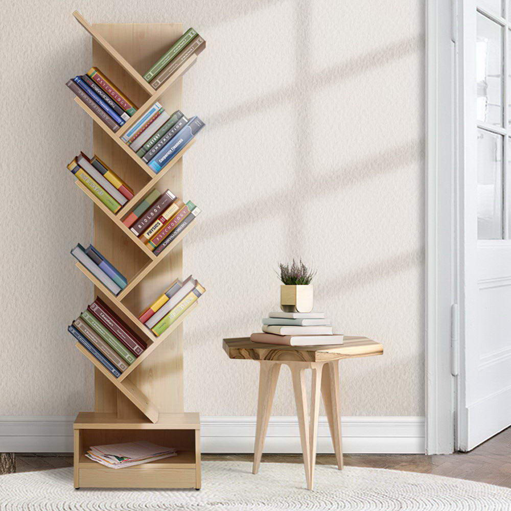 Natural wood tree bookshelf filled with books in neutral room with wooden side table, three-quarter angle view