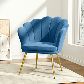 Navy blue velvet shell-back armchair with scalloped backrest and gold metal legs in lifestyle room with window