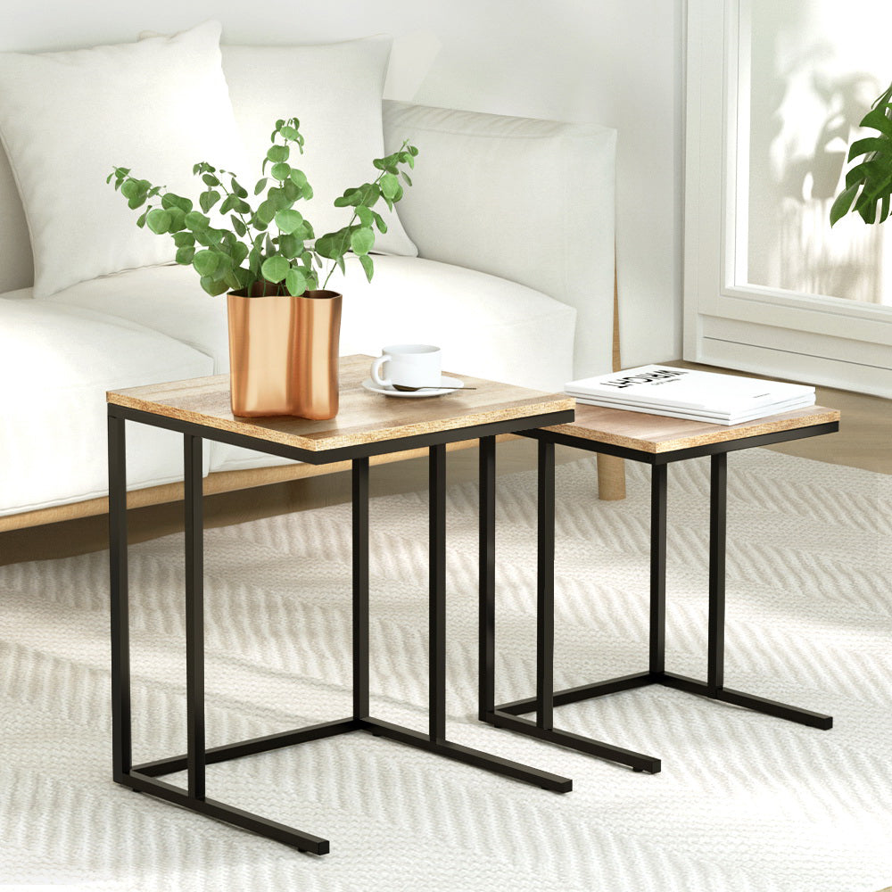 Set of two nesting C-shaped side tables with oak wood grain tops on black metal frames beside a white sofa, styled with