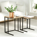 Set of two nesting C-shaped side tables with oak wood grain tops on black metal frames beside a white sofa, styled with