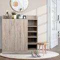 Oak finish 2-door shoe cabinet with side open shelves in entryway with round mirror and floor lamp