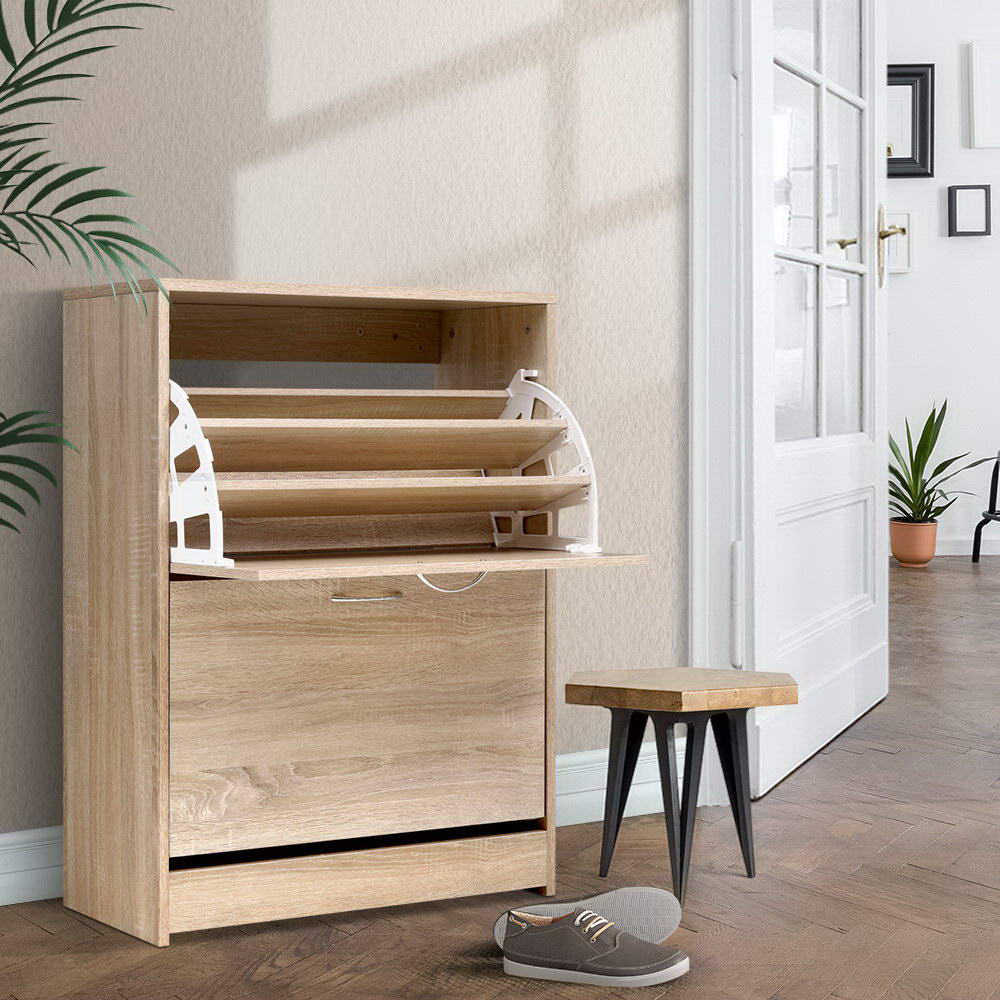 Oak two-door flip-out shoe cabinet top compartment open showing empty tray mechanism in hallway with wooden stool and shoes