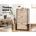 Oak finish three-tier flip-out shoe cabinet with black metal frame in living room lifestyle with umbrella stand and sofa