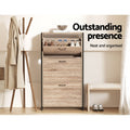 Oak three-tier shoe cabinet with black metal frame top door open showing stored shoes in hallway lifestyle with coat rack