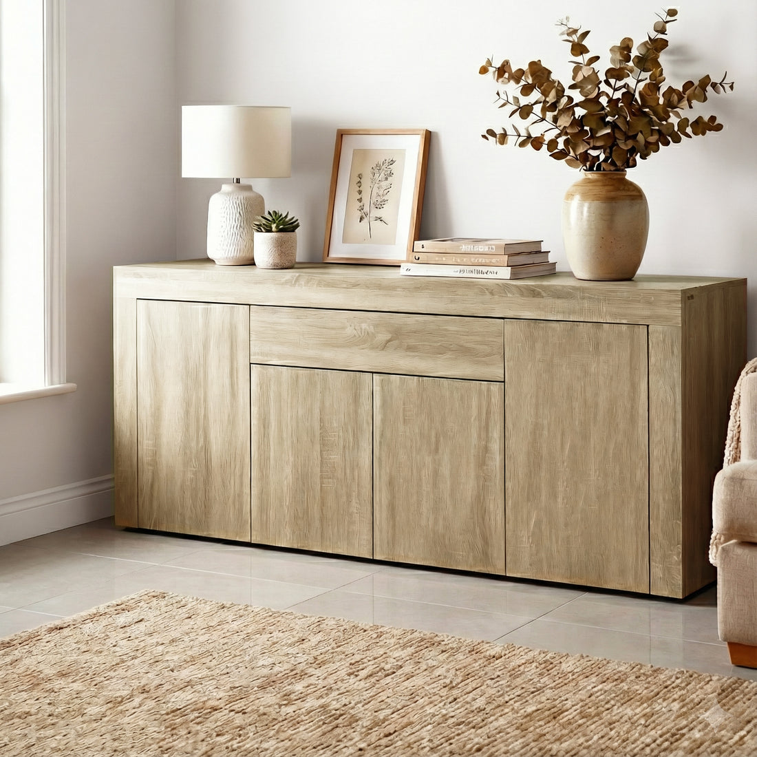 Oak buffet sideboard in living room with lamp, framed art, books and eucalyptus vase on top, jute rug on tile floor