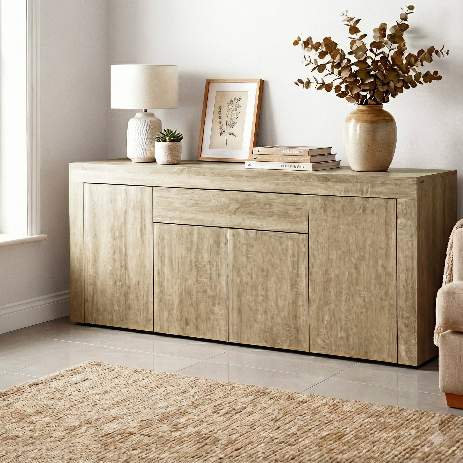Oak buffet sideboard in living room with lamp, framed art, books and eucalyptus vase on top, jute rug on tile floor