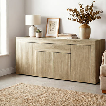 Oak buffet sideboard in living room with lamp, framed art, books and eucalyptus vase on top, jute rug on tile floor